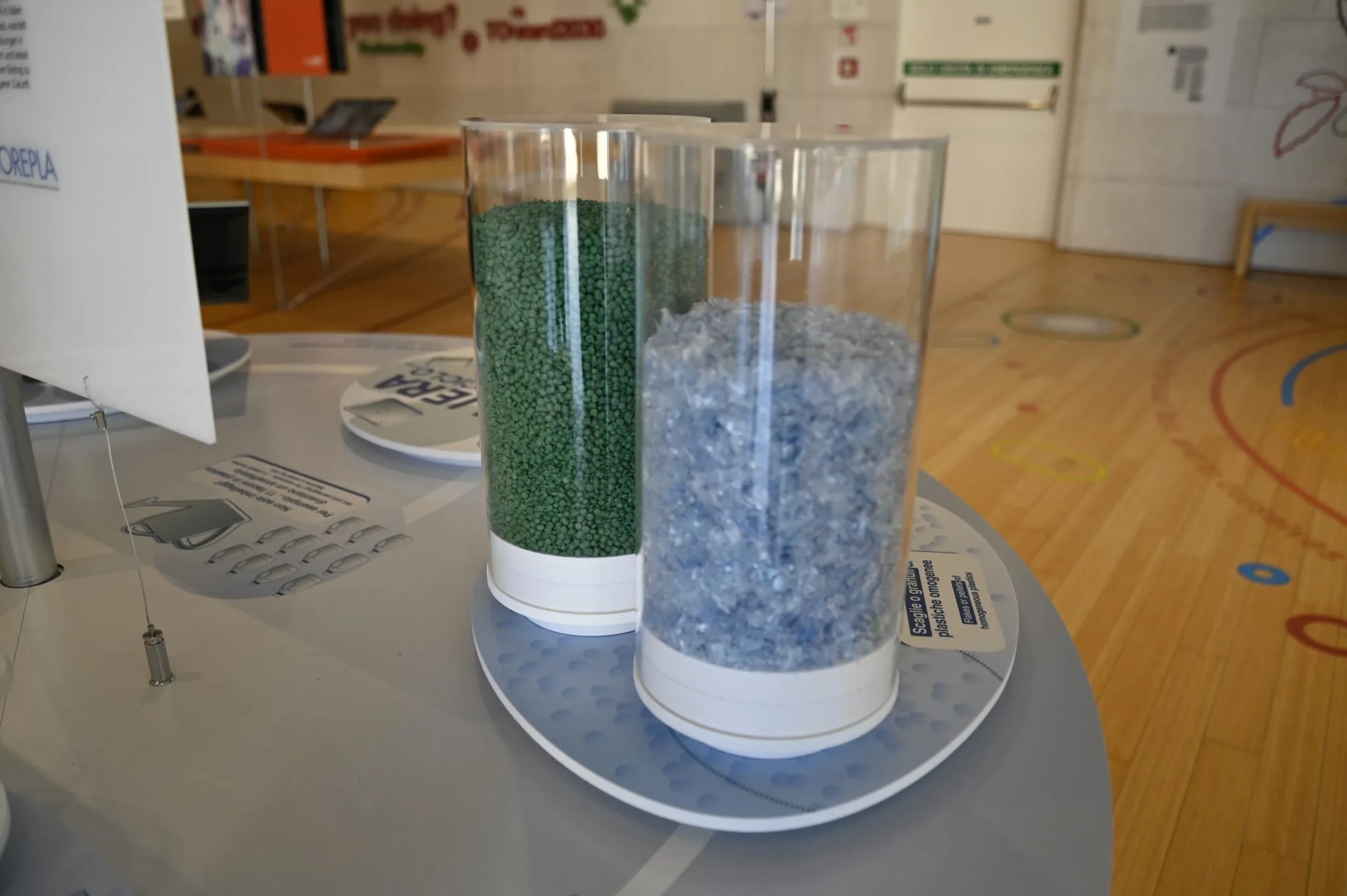 Cilindri con granuli e scaglie di plastica riciclata esposti nell'exhibit